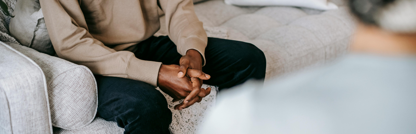 Therapist and client sitting in therapist office, client on couch with clasped hands.